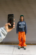 Model wearing blue washed Saint Vanity university crewneck with orange trousers